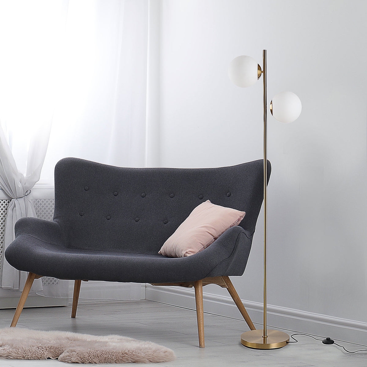 Gold floor lamp with two white glass globes beside a gray sofa