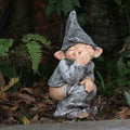 Grey resin naughty gnome statue in a garden bed