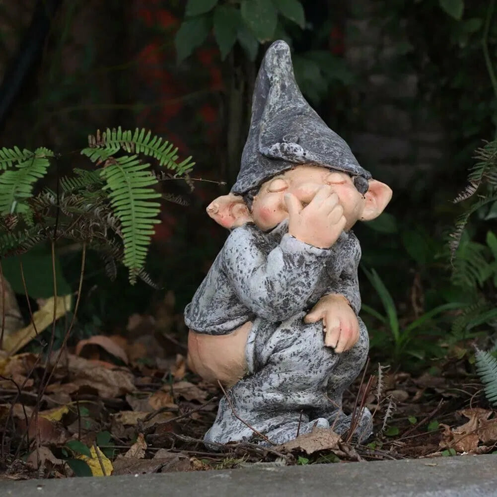 Grey resin naughty gnome statue in a garden bed