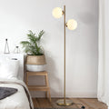 Brass floor lamp with two white glass globe shades beside a bed